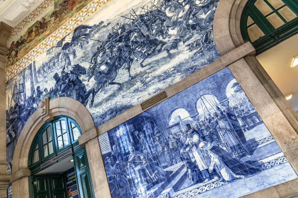 Blue and white azulejo tile murals depicting historical scenes, displayed on the walls of a traditional portuguese train station.