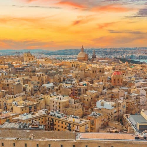 Aerial view of valletta, malta at sunset, featuring dense historic buildings and the prominent dome of st. paul's pro-cathedral against a vibrant sky.