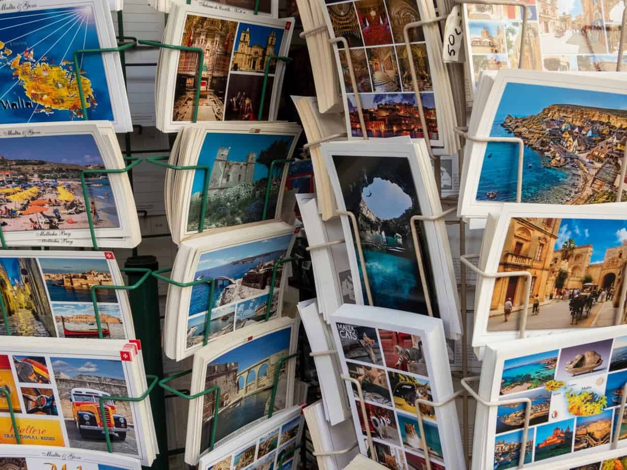 A display stand in Malta filled with various postcards depicting scenic views of architecture, landscapes, and cityscapes.