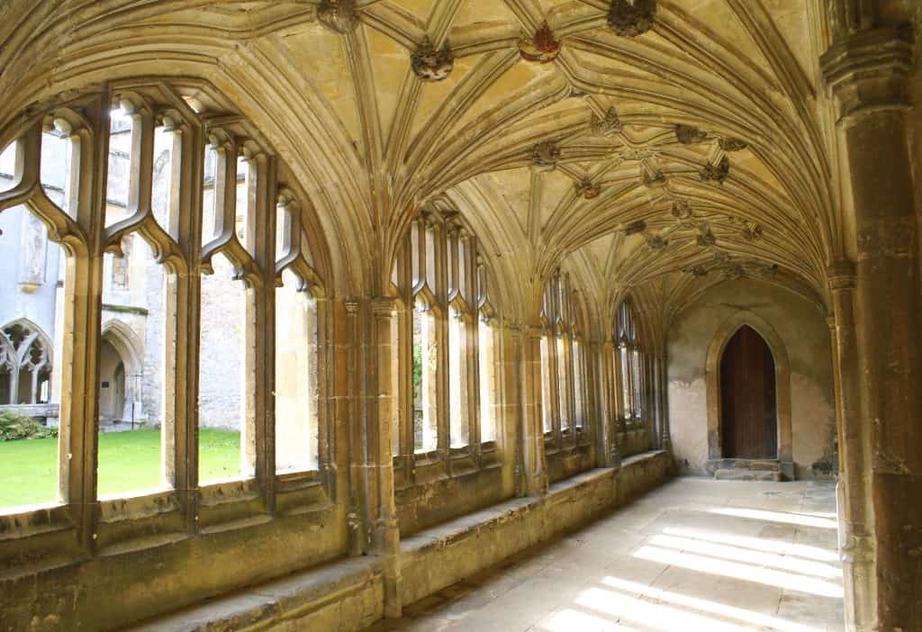 Gothic cloister with vaulted ceilings and arched windows overlooking a grassy courtyard.