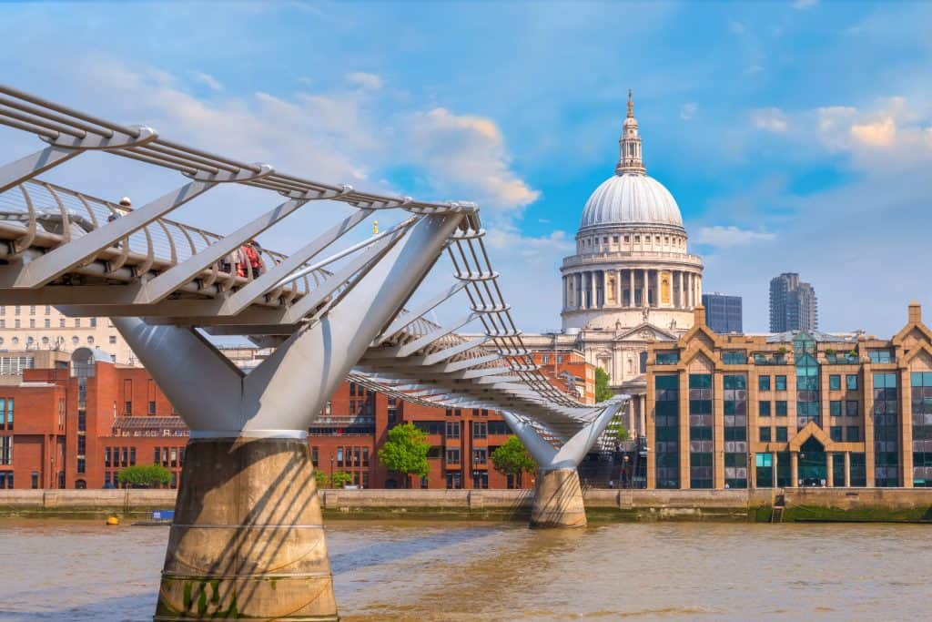 Millennium Bridge over the River Thames with St. Paul’s Cathedral in the background under a blue sky.