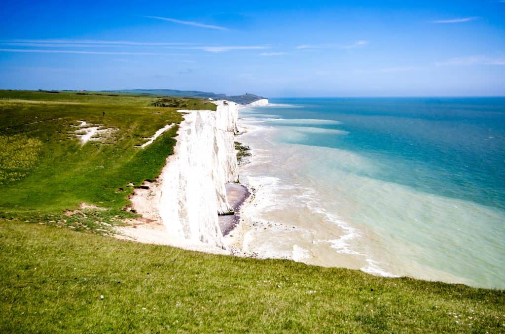 Cliffside view of the Seven Sisters in England, with white chalk cliffs, green grass, and the blue sea under a clear sky.