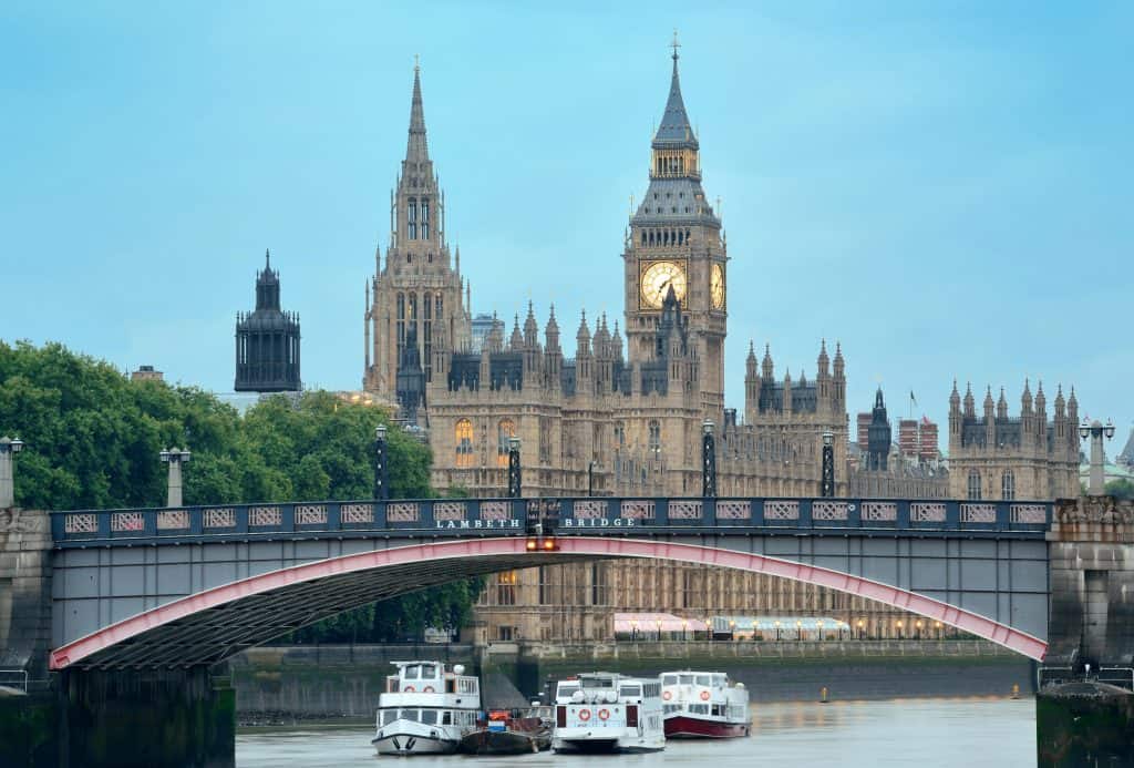 View of the Houses of Parliament with Big Ben and Westminster Bridge spanning the River Thames in London, under a cloudy sky.
