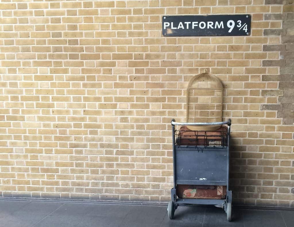 A luggage cart half-embedded in a brick wall under a sign reading "Platform 9¾.