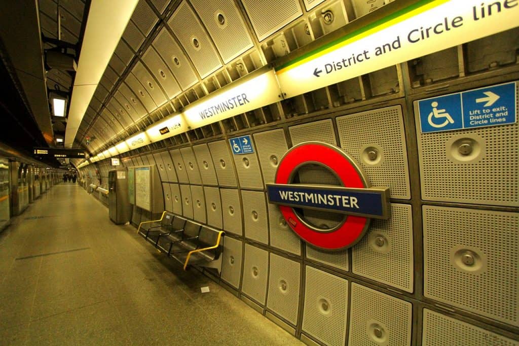 Underground station platform with "Westminster" sign. Includes accessibility symbols, seating area, and overhead directional signs for District and Circle lines.
