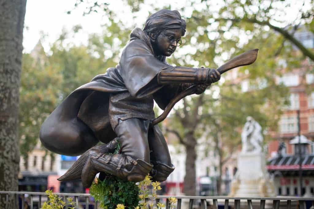Explore the enchanting bronze statue of a young wizard flying on a broomstick, nestled in an outdoor park with trees and buildings in the background—an iconic stop for Harry Potter fans seeking magical things to do in London.