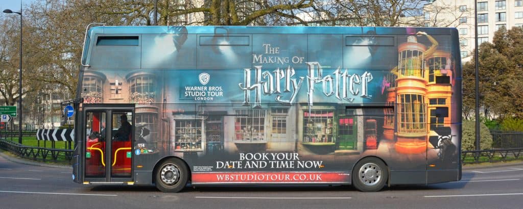 A double-decker bus wrapped in Harry Potter-themed graphics highlights one of the top Harry Potter things to do in London: "The Making of Harry Potter" tour by Warner Bros Studio Tour London.