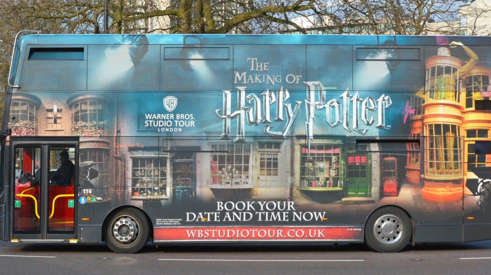 A double-decker bus wrapped in Harry Potter-themed graphics highlights one of the top Harry Potter things to do in London: "The Making of Harry Potter" tour by Warner Bros Studio Tour London.