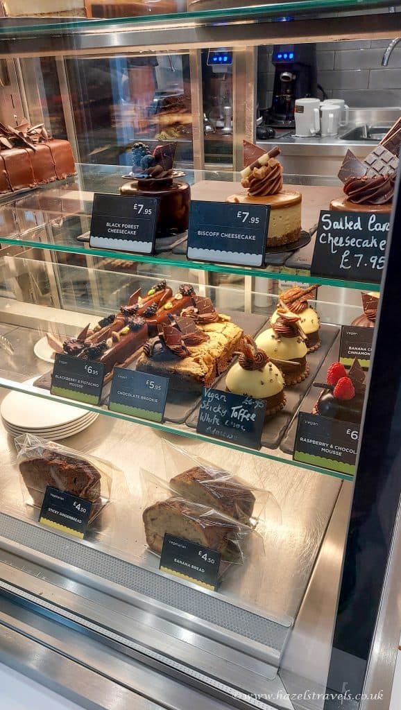 Display case with assorted desserts, including cheesecakes and cakes, labeled with prices in euros.