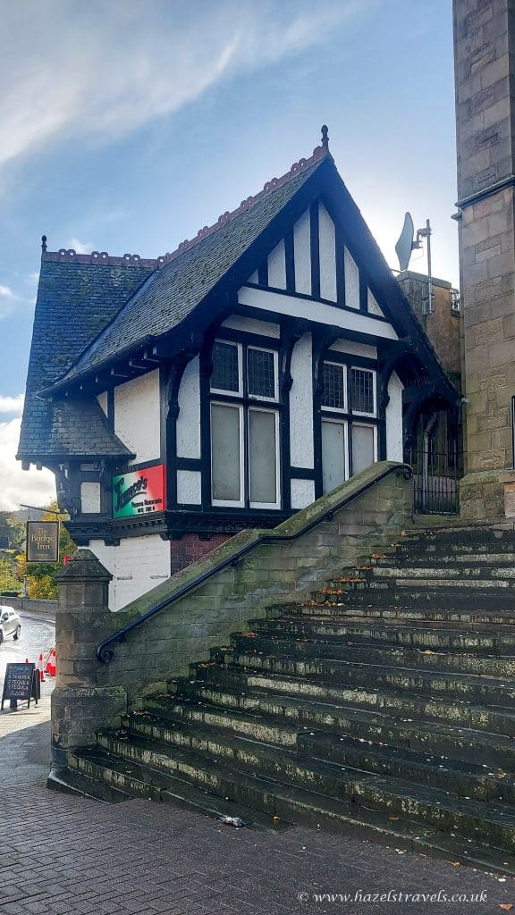 A small, black-and-white Tudor-style building with steep stone steps leading up to it. A sign shows "James' Bar." The sky is partly cloudy.