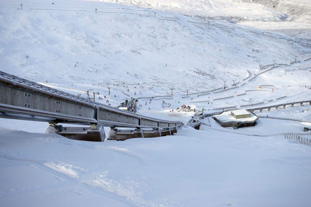 Snowy ski resort with ski lifts and scattered skiers on a white, mountainous landscape near Aviemore in Scotland.