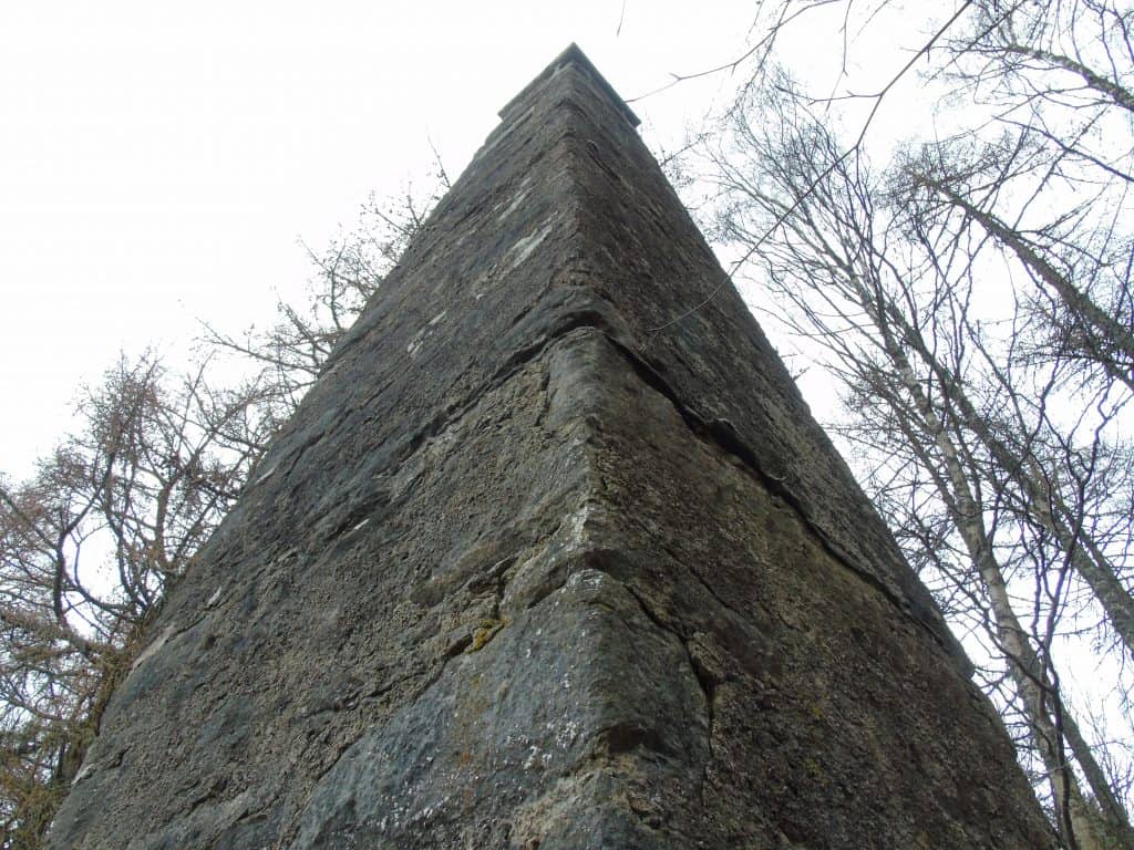 A tall stone wall seen from below, with bare trees surrounding it against a cloudy sky, in the grounds of Blair Castle