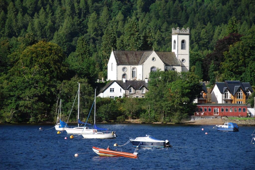 Boats on a loch near Pitlochry with a church and houses in the background, surrounded by trees.