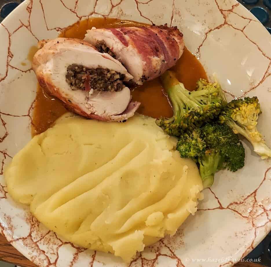 Plate with sliced bacon-wrapped haggis-stuffed chicken (a food od Scotland), mashed potatoes, broccoli, and sauce.