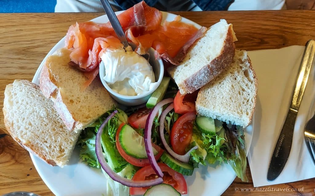 Plate with Scottish smoked salmon, bread slices, cream cheese, and a side salad of mixed greens, tomatoes, cucumber, and red onion. Knife and fork on the right.