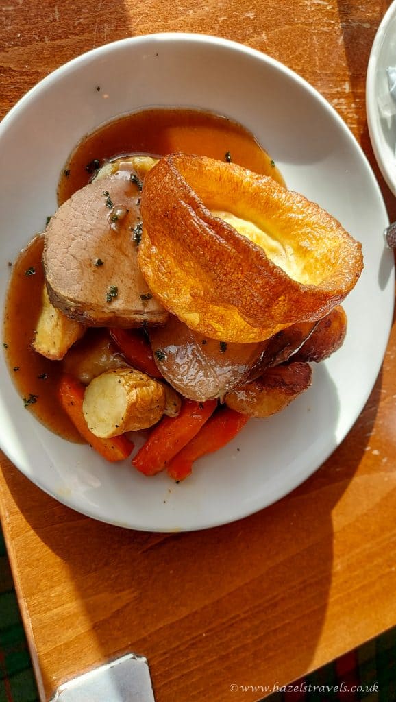 A plate of roast beef, Yorkshire pudding, roasted potatoes, and carrots topped with gravy.