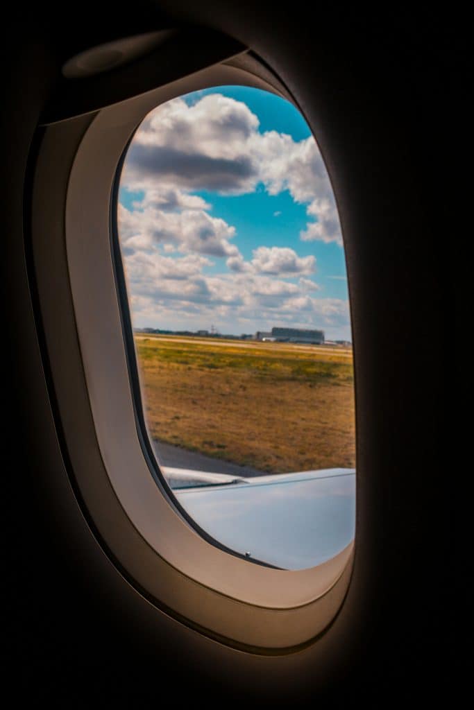 View through an airplane window showing a runway and grassy field under a sky with scattered clouds.