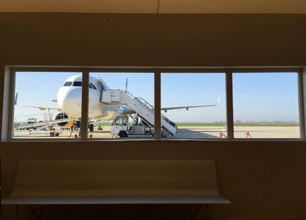 View through a window of an airplane parked on the tarmac with boarding stairs attached.