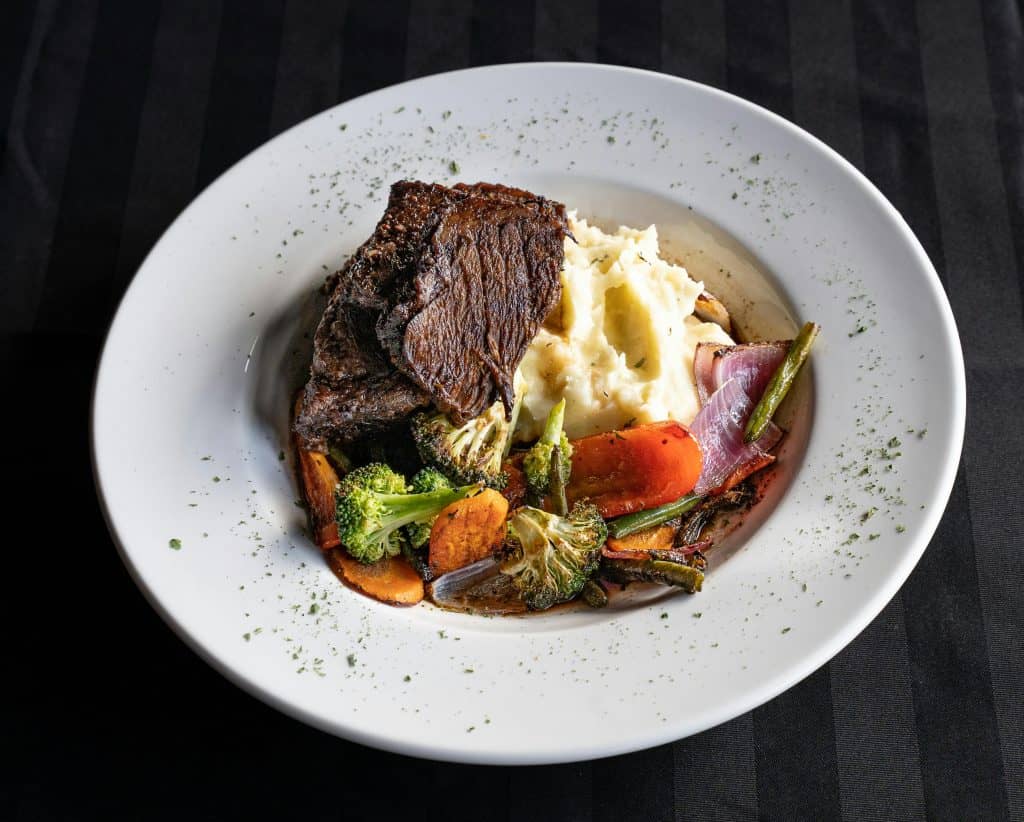 Grilled steak on a plate with mashed potatoes and assorted vegetables, including broccoli, carrots, and onions, garnished with herbs.