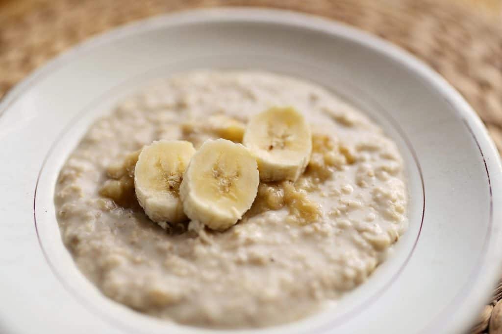 A bowl of oatmeal topped with banana slices on a white plate.