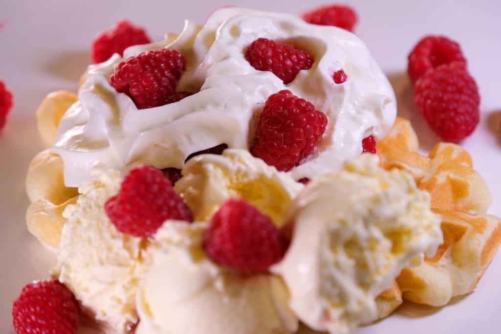 Waffles topped with whipped cream, raspberries, and a scoop of vanilla ice cream on a plate.