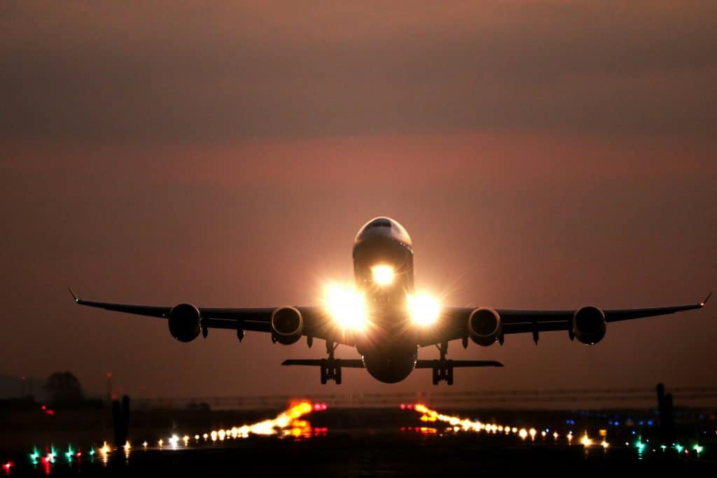 Airplane taking off from a runway with illuminated lights during sunset.