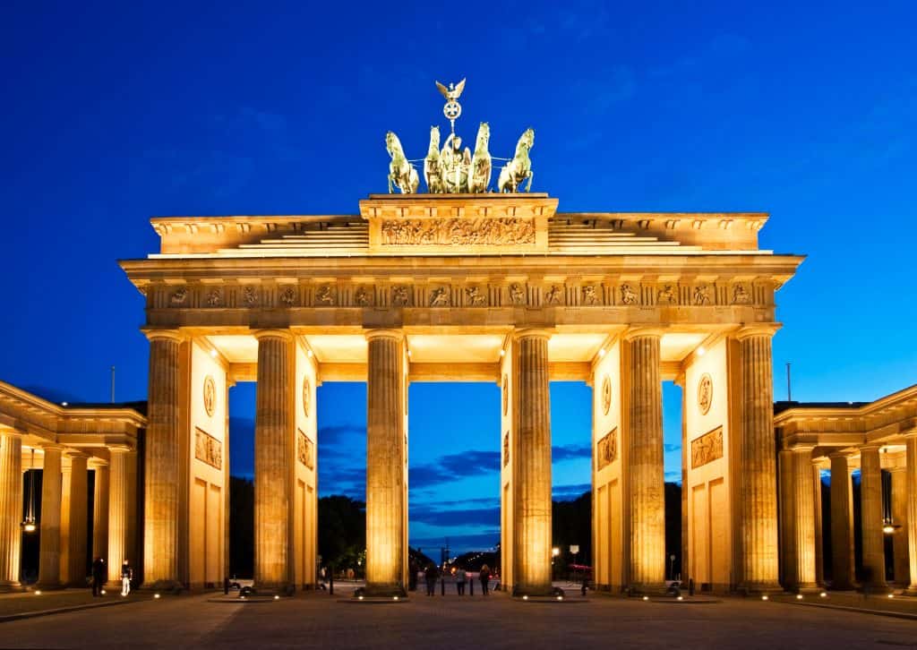 The Brandenburg Gate at dusk, illuminated with golden lights against a deep blue sky.
