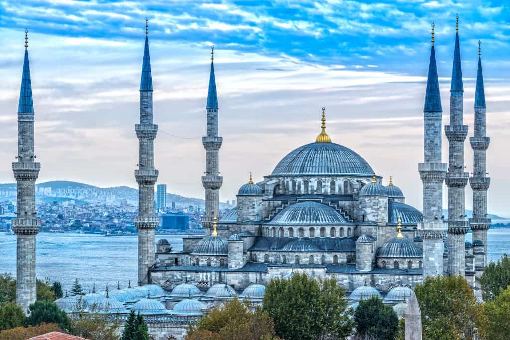 Blue Mosque with six minarets and multiple domes, set against a cityscape and a partly cloudy sky, viewed from a distance.