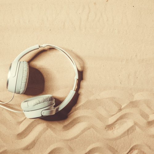 White headphones lying on textured sand, with visible wavy patterns.