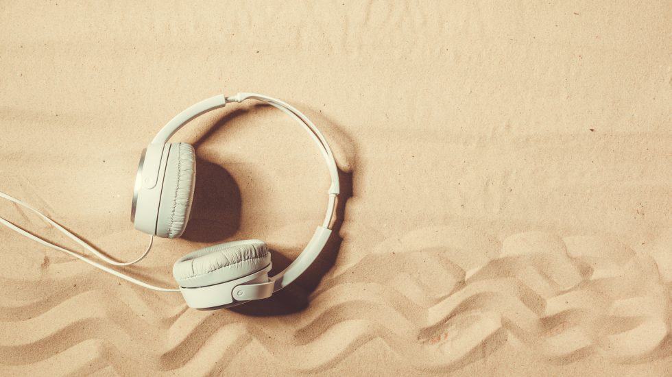 White headphones lying on textured sand, with visible wavy patterns.