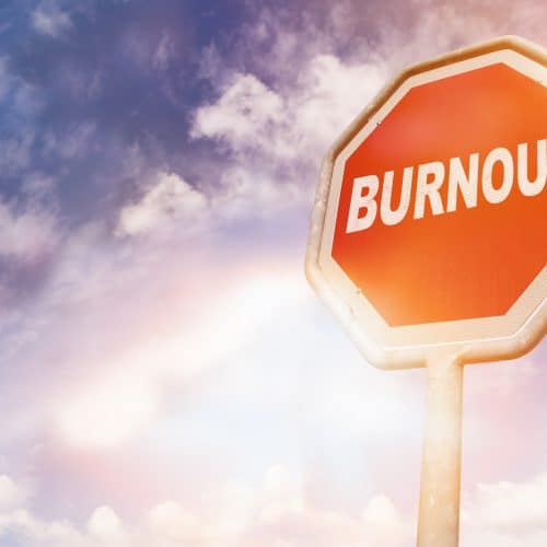 A stop sign with "BURNOUT" written on it stands against a cloudy sky.