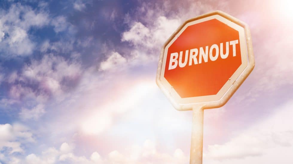 A stop sign with "BURNOUT" written on it stands against a cloudy sky.