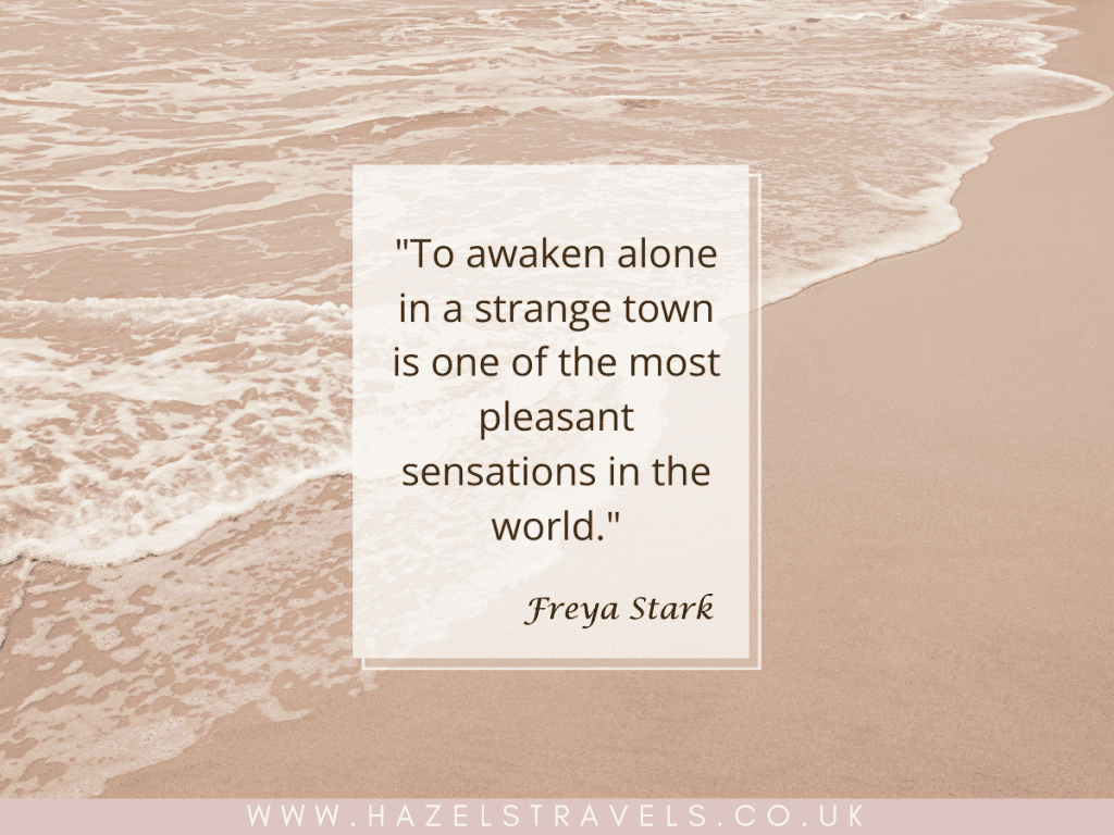 Quote on a beach background: "To awaken alone in a strange town is one of the most pleasant sensations in the world." - Freya Stark.