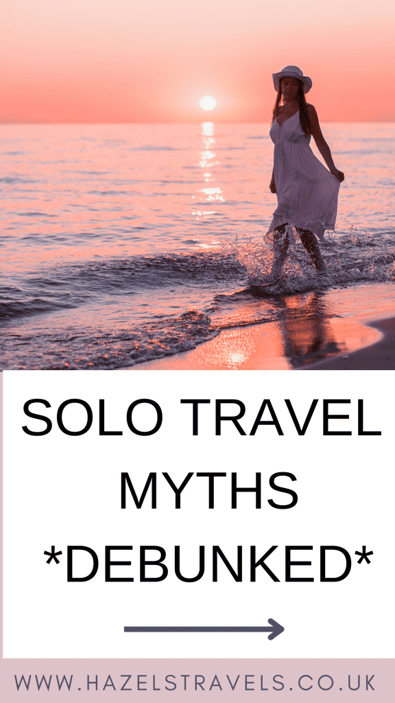 Woman in a white dress and hat walks on the beach as the sun sets. Text below reads: "Solo Travel Myths *Debunked*" with a website URL.