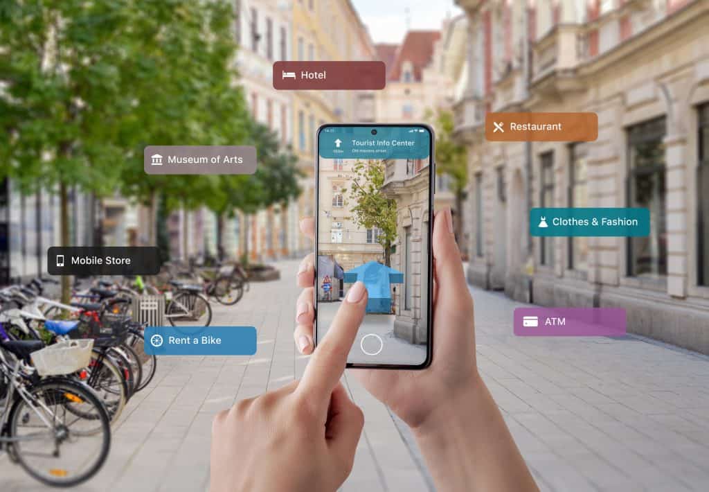 Hands hold a smartphone showing augmented reality navigation in a city street. Icons display nearby locations: hotel, restaurant, museum, mobile store, bike rental, fashion, ATM.
