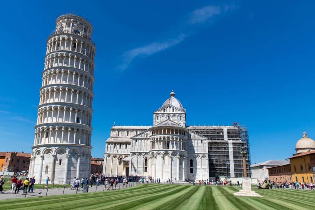 The Leaning Tower of Pisa with the adjacent cathedral in Piazza dei Miracoli under a clear blue sky.