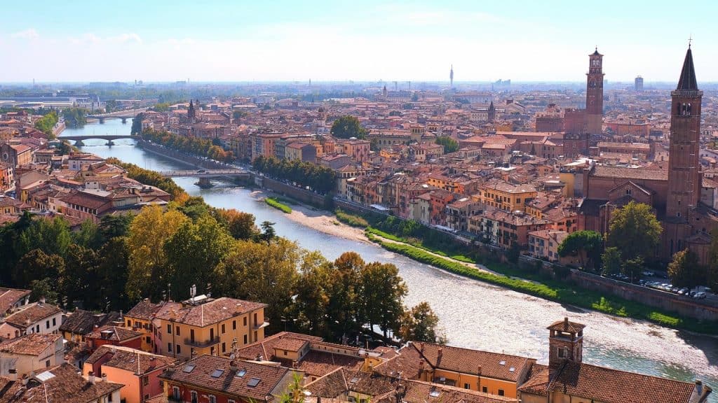 Breathtaking aerial view of Verona, Italy, showcasing the Adige River, historic old town, and famous landmarks like Torre dei Lamberti and Verona Cathedral in a vibrant cityscape.