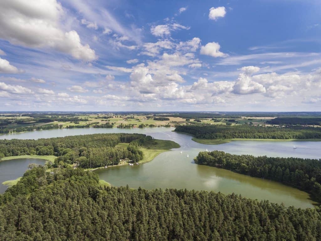 Aerial view of a landscape with interconnected lakes, dense forests, and a partly cloudy sky, creating a serene natural scene.