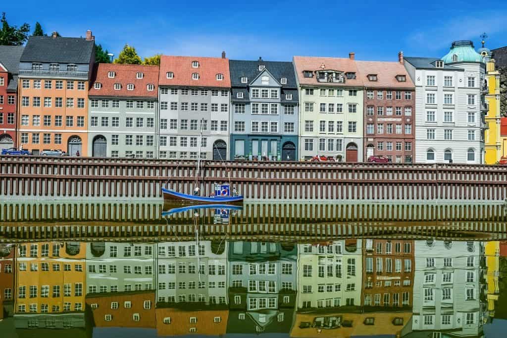 Colourful Scandinavian waterfront houses reflecting on the water in Bergen, Norway. A small boat is docked along the quay, showcasing picturesque European harbour scenery and architecture.