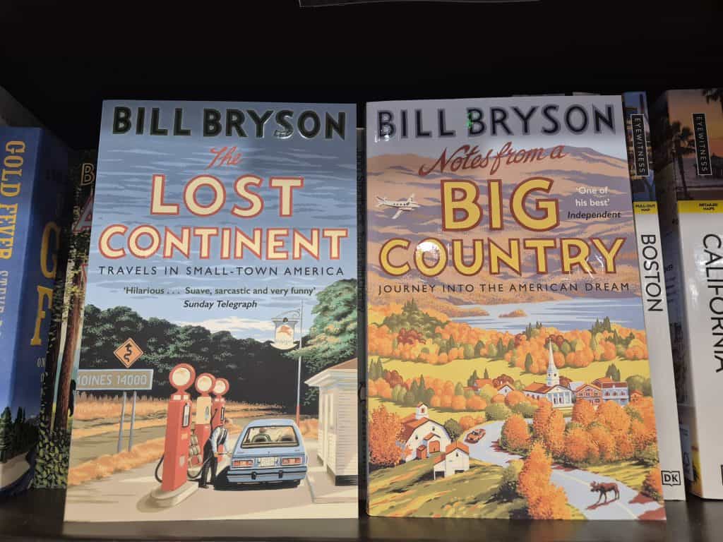 Two Bill Bryson books are displayed on a shelf: "The Lost Continent" and "Notes from a Big Country," both featuring illustrated covers with American themes.