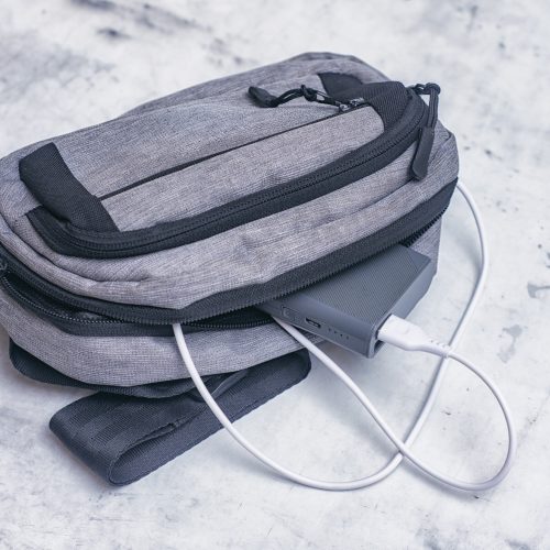 Rechargeable power bank connected to a grey backpack for travel.