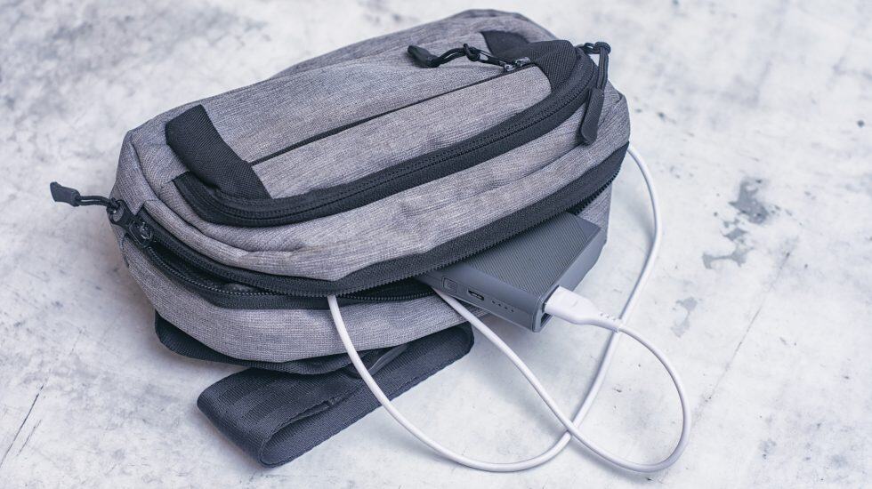 Rechargeable power bank connected to a grey backpack for travel.