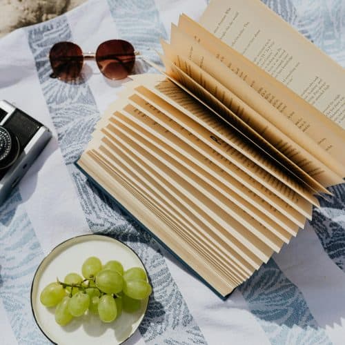 Relaxing beach holiday travel planning with a camera, sunglasses, and travel guides on a sunlit seaside setting.