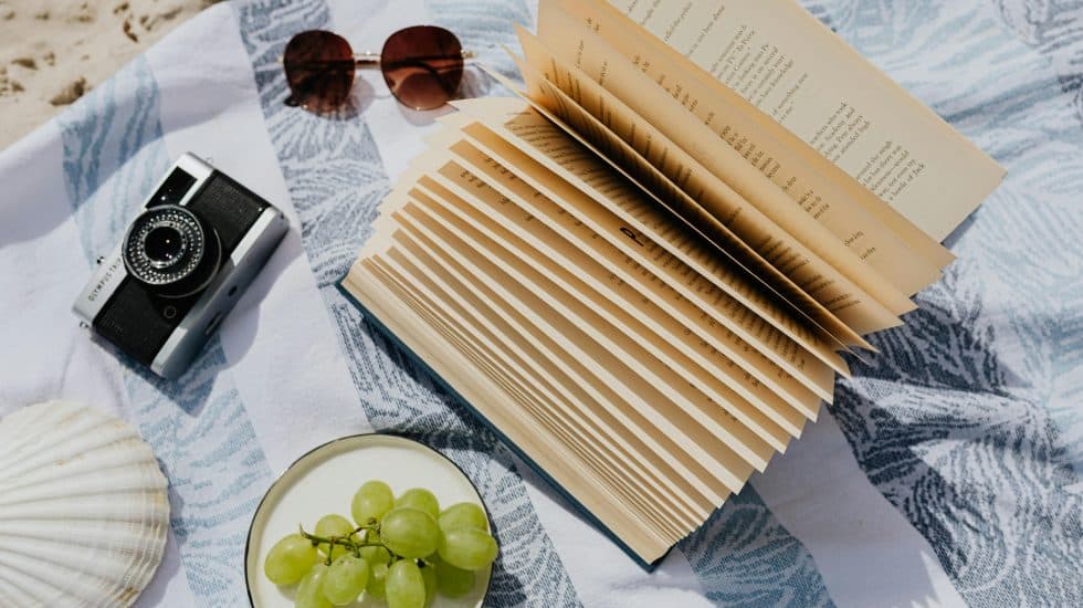 Relaxing beach holiday travel planning with a camera, sunglasses, and travel guides on a sunlit seaside setting.