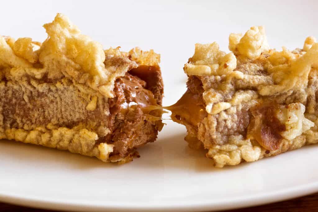 A close-up of a deep-fried chocolate bar split in half, showing melted chocolate inside, on a white plate.