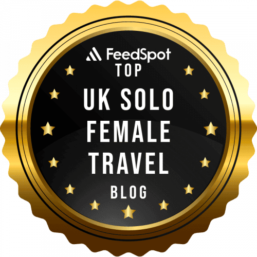 A gold and black badge displaying "FeedSpot Top UK Solo Female Travel Blog" with stars and a scalloped edge.