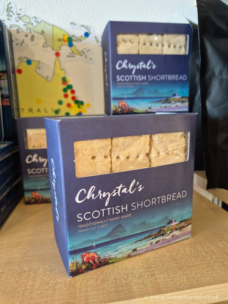 Boxes of Chrystal's Scottish Shortbread, traditionally handmade, are displayed on a shelf. The packaging is blue with an illustration and clear window showing the shortbread inside.