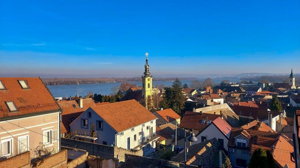 Stunning aerial view of a historic European town with red-tiled roofs, a church steeple, and a river backdrop, showcasing scenic architecture and tranquil surroundings.