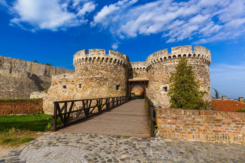 Medieval stone castle entrance with wooden bridge, historic fortress in France, blue sky, sunny day, popular travel destination, Hazel’s Travels.