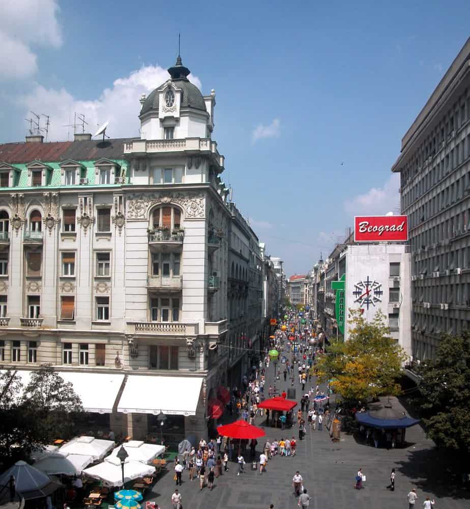 Busy Knez Mihailova Street in Belgrade on a sunny day, with historic buildings, outdoor cafés, and crowds of people walking along the pedestrian zone